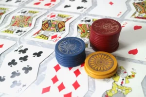A close-up shot of a baccarat table showing stacks of blue and red casino chips with scattered playing cards, including the eight of clubs and eight of diamonds.